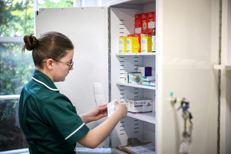 Treloar's medicine management technician, stands in front of a cabinet of medication, checking a label on a packet.