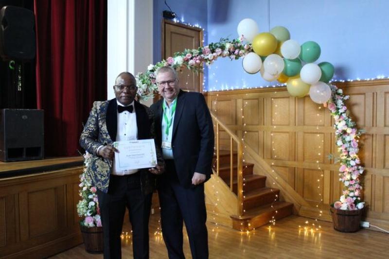 Independent Governor Rob Darracott present Treloar staff member with certificate at staff celebration event, posing underneath a flower decorated archway.