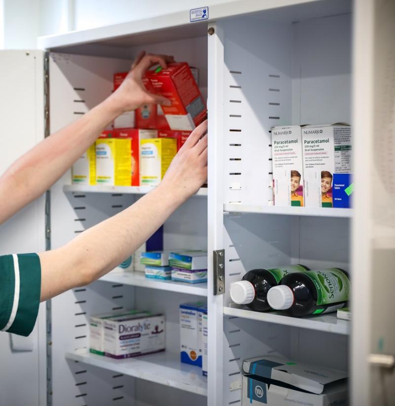 Pharmacist organizing various medication boxes and bottles inside a white medicine cabinet.