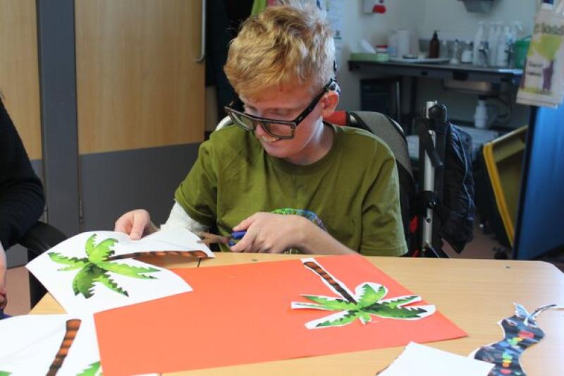 Treloar's student in a green shirt sitting at a table cutting out paper palm tree shapes for a craft project.