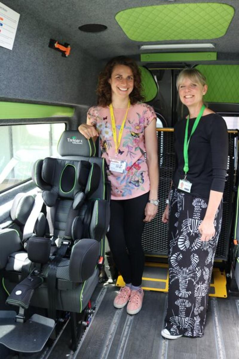 two women inside a minibus, stand next to an adapted car seat to enable Treloar's primary students to travel safely