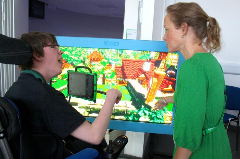 Treloar's student in front of a big screen displaying a colourful video game with a teacher in a green dress having a discussion about the game.