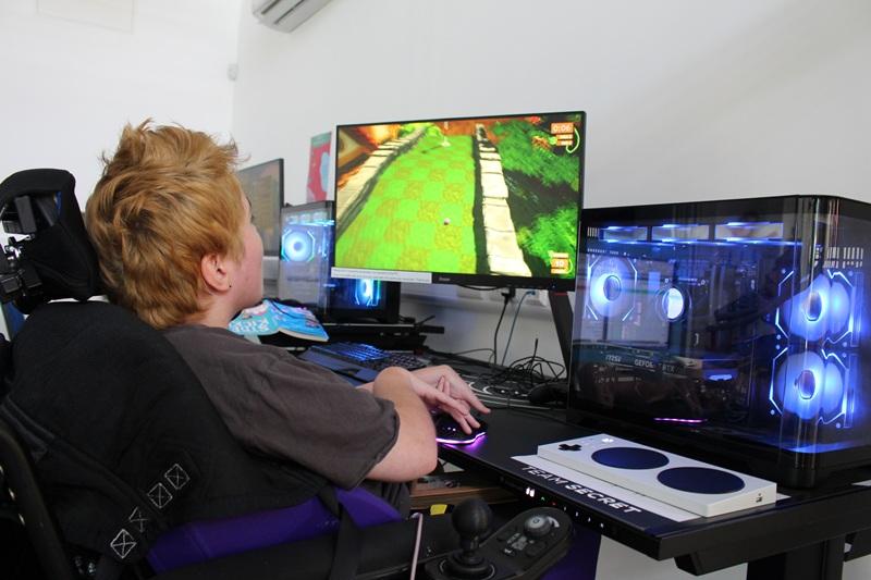 Treloar's student playing a colourful video game on a desktop computer with blue LED lights in a modern setup.