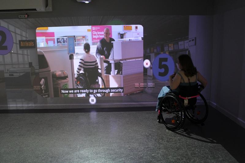 Treloar College student watching a video projected on a wall showing airport security screening with subtitles.