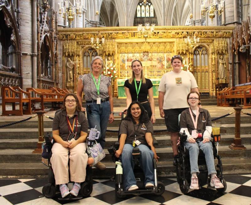 Group of six people, including three in wheelchairs, posing inside a grand cathedral with ornate golden altar in the background.