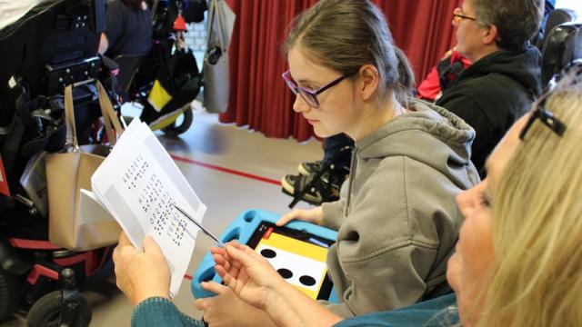 In assembly, Treloar School student is looking at a braille book together with her support assistant.