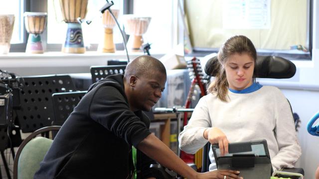 Treloar College student using her iPad to play Clarion; she is focused and looking at her screen; her assistant is sitting next to her and looking at the screen.
