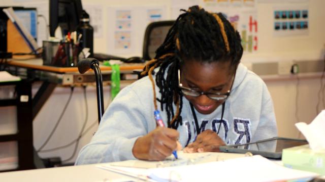 Treloar College student at her desk in the classroom, completing a written task; she looks focused and happy.