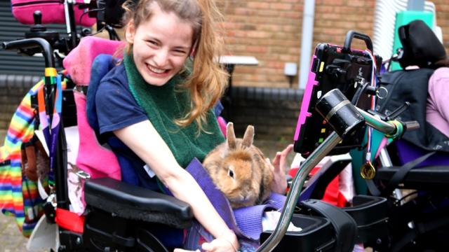 Treloar College student is smiling to the camera: there is a pet rabbit on her lap; the student is really happy with the experience.