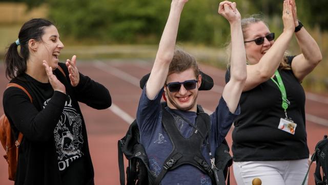 Treloar College student cheering on, raising his both arms up in the air - his 2 assistants are walking next to him and clapping. Everyone is having fun.