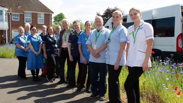Treloar’s Nursing and Healthcare Team lined up outdoors posing for a group photo. It's a sunny day and behind them, there is a row of wild blue and red flowers.