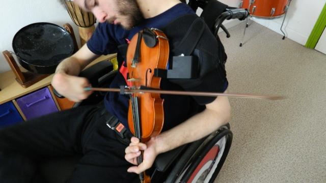 Treloar's student playing a violin using a bow guide and an adapted shoulder support