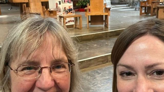 A selfie taken by 2 Treloar's Speech and Language Therapists, Emily Ball and Caroline Weighton, at a special non-denominational Anniversary event at Southwark Cathedral. A banner of the event in the background. Emily and Caroline are smiling to the camera. 