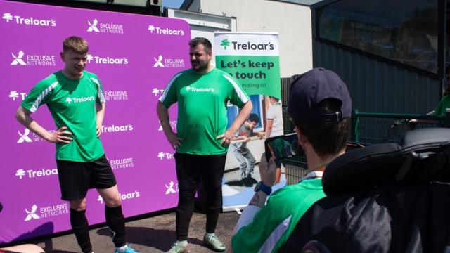 Treloar's student is conducting a pitch-side interview with 2 Treloar's staff members - both wearing green, branded Treloar's T-shirts.