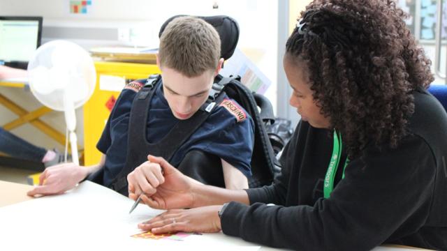 A student support assistant assisting Treloar College student with drawing by holding his hand. Both are focused on the task.