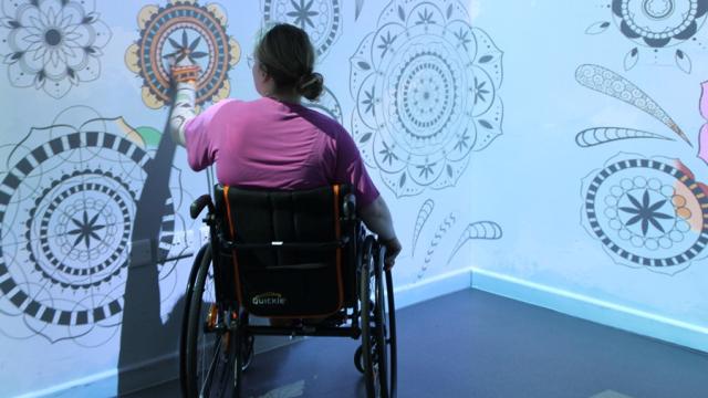 Treloar College student wearing a pink shirt and is interacting with intricate black and white mandala designs projected on the wall.