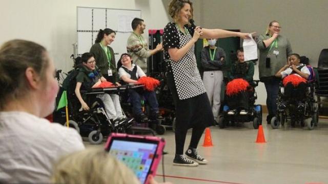 Head of School Lisa Bond holding a microphone, leading the pancake day event in the school hall with students watching from the side lines
