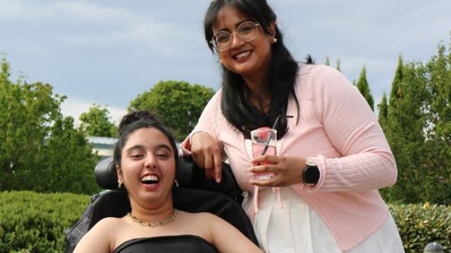 Treloar School student in a black dress with a green belt on her [prom day with her assistant. Both happy and smiling at the camera.
