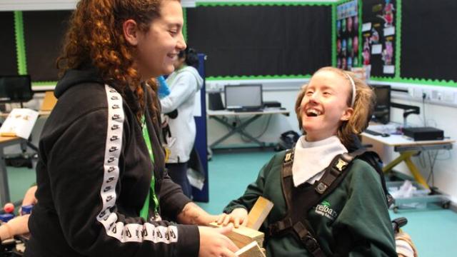 student smiling with support assistant, using bricks to balance