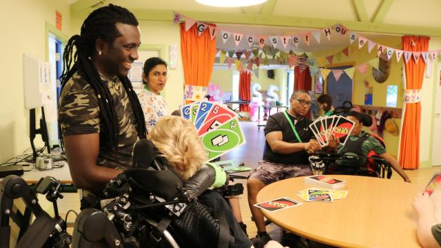 students and 2 staff play uno with extra large cards. They are smiling and seated around a large round table