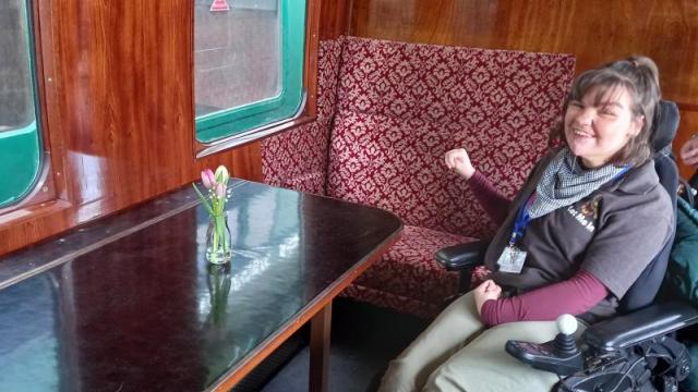 College student poses beside folding table on The Watercress Line accessible railway carriage