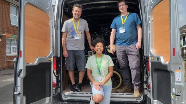Treloar's staff member with 2 men, all wearing lanyards stand and sit at the open back of a white van under a cloudy sky.