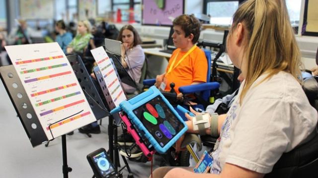 Treloar's student using a tablet to play the clarion in a classroom setting with music sheets on stands nearby.