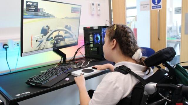 Treloar's student playing a racing video game on a desktop computer with a large monitor in a bright room.