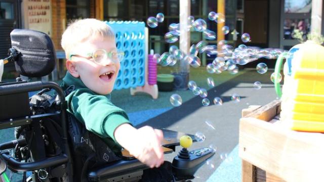 Treloar's primary student joyfully reaching out to catch floating soap bubbles outdoors on a sunny day.