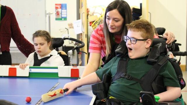 Treloar's student playing table cricket with assistance from his assistant. His mouth is open as he gets excited about the game.