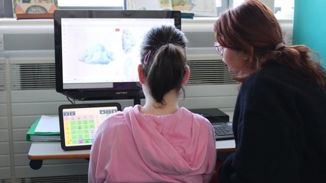 Treloar's student in a pink hoodie and her student support assistant with glasses looking at a computer screen displaying a cloud image in a classroom setting.