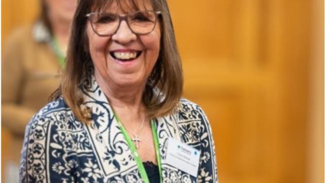Photo of Cheryl Brewer Chair of Trustees Treloar Trust, she is wearing a blazer and a green lanyard, smiling towards the camera