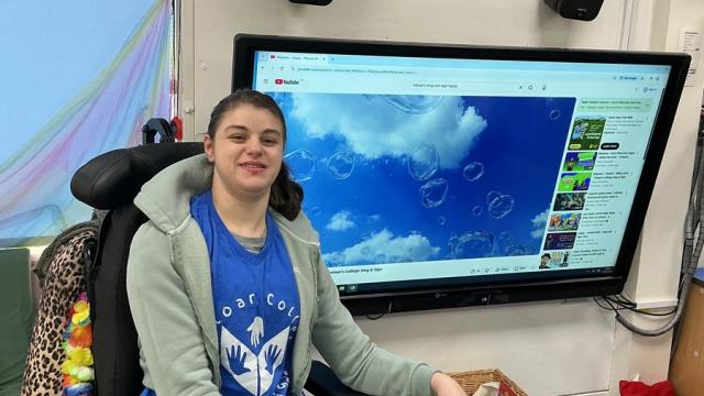 Treloar College student in front of a large screen displaying a YouTube video of bubbles against a blue sky.