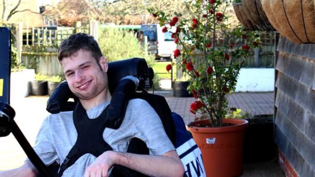Treloar College student outdoors near a potted rose bush on a sunny day. He is smiling and posing for a photo.