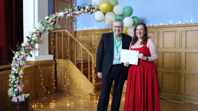 Independent Governor Rob Darracott present Treloar staff member with certificate at staff celebration event, posing underneath a flower decorated archway.