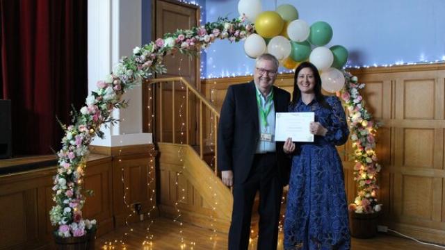 Treloar's staff celebration event, Governor Rob Darracott presents Treloar's staff member with a certificate under a flower decorated archway