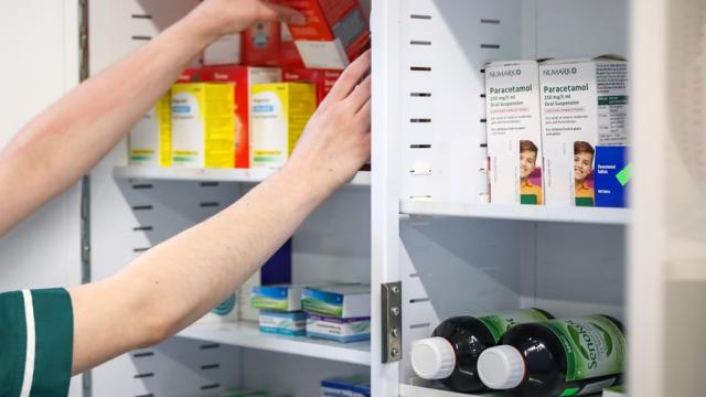 Pharmacist organizing various medication boxes and bottles inside a white medicine cabinet.