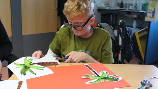 Treloar's student in a green shirt sitting at a table cutting out paper palm tree shapes for a craft project.