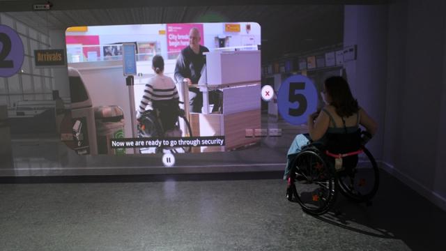 Treloar College student watching a video projected on a wall showing airport security screening with subtitles.