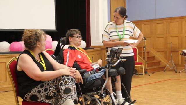 Student in a wheelchair speaks with staff member in School hall