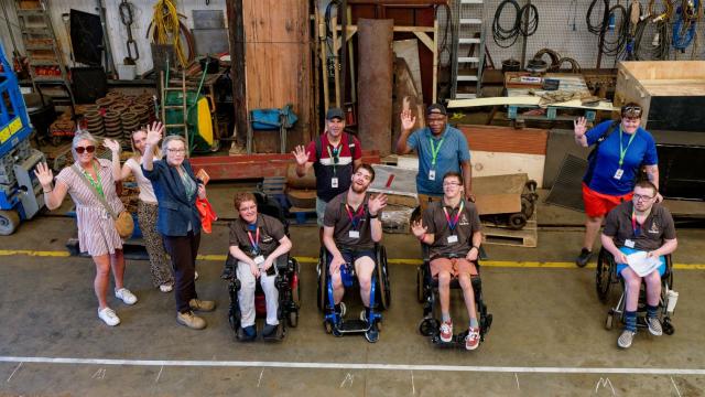 A group of students in wheelchairs in a heritage railway workshop, with an outline of a carriage marked out on the floor