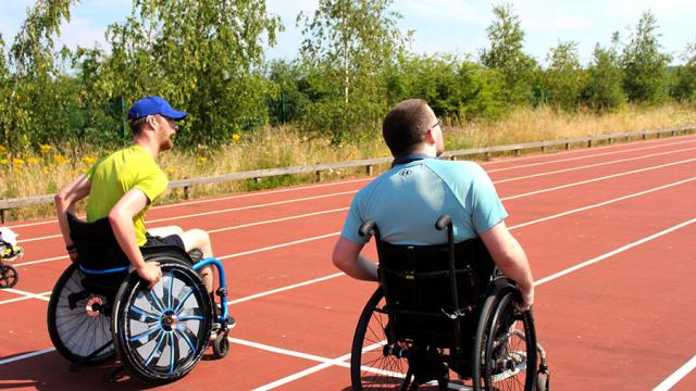 Two Treloar College students preparing to race on an outdoor sport track under a clear sky. It is a sunny and warm day. The boys are wearing T-shirts.