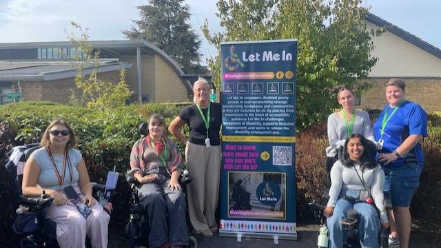 Group of college students in wheelchairs with a pull up banner promoting Let Me In student enterprise