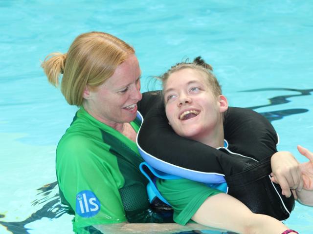 Treloar's student in the pool with her support assistant; the student is in the pool, being held by her assistant. Both are smiling at each other and having a good time.