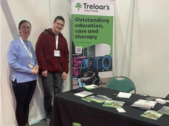 Maria Sherwood, Treloar's Progress and Transition Team Manager at Naidex with former student Eoin standing by Treloar's exhibition stand with branded merchandise.