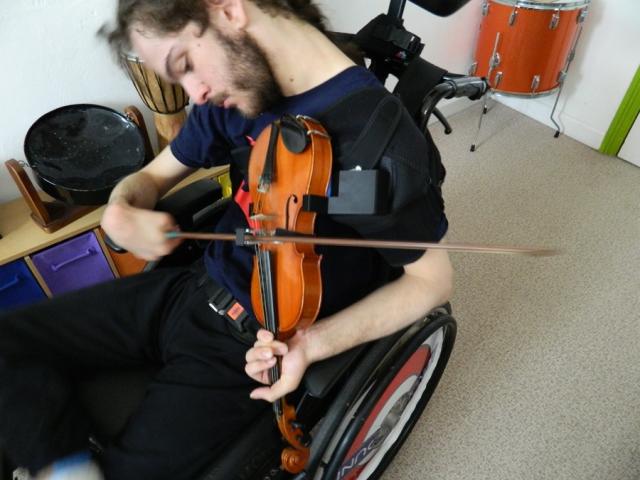 Treloar's student playing a violin using a bow guide and an adapted shoulder support