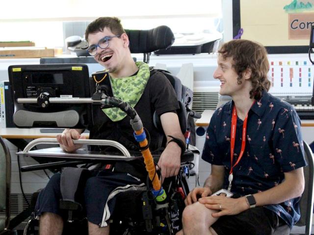 Oliver Squibb, Clarion Peripatetic Teacher during a music workshop, sitting next to Treloar's student who is using Clarion - both are happy and are smiling.
