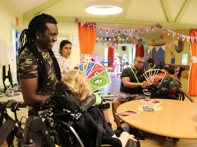 students and 2 staff play uno with extra large cards. They are smiling and seated around a large round table