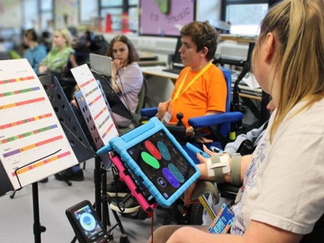 Treloar's student using a tablet to play the clarion in a classroom setting with music sheets on stands nearby.