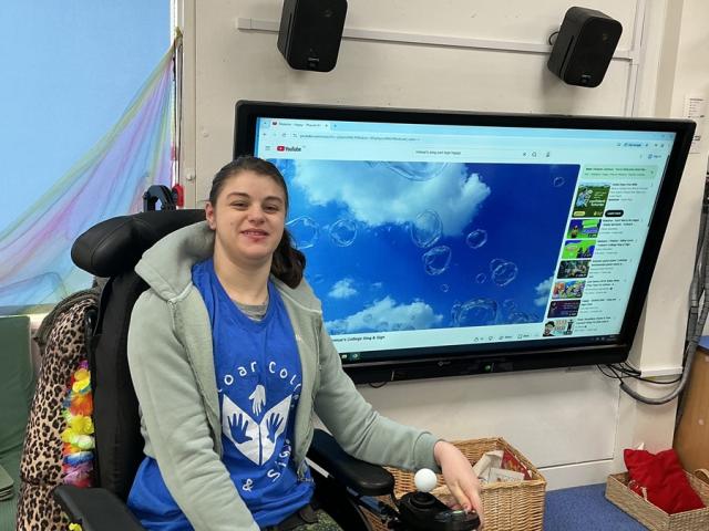 Treloar College student in front of a large screen displaying a YouTube video of bubbles against a blue sky.
